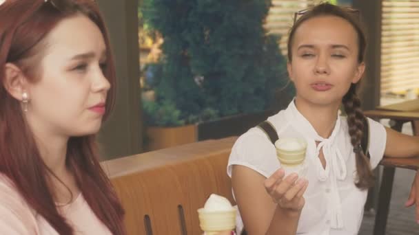 Dos mujeres jóvenes comen helado, se sientan en un café al aire libre, se divierten. 4k, cámara lenta, steadicam . — Vídeo de stock