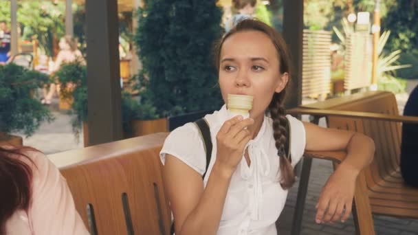 两个年轻的妇女吃冰淇淋, 坐在一个户外咖啡馆, 他们有乐趣。4k. 慢动作, 替身. — 图库视频影像