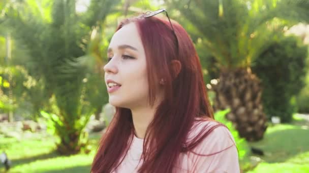 Jovem bela menina ruiva dançando no parque. mulher em uma mini saia dançando em um parque tropical em um fundo de palmas. 4k, câmera lenta — Vídeo de Stock