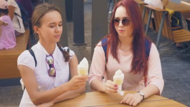 İki genç kadın açık bir kafede oturup dondurma yemek, eğleniyorlar. 4k, ağır çekim, steadicam.