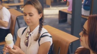 İki genç kadın açık bir kafede oturup dondurma yemek, eğleniyorlar. 4k, ağır çekim, steadicam.