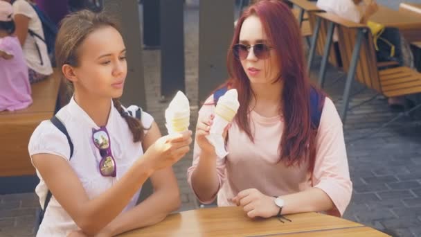 Dos mujeres jóvenes comen helado, se sientan en un café al aire libre, se divierten. 4k, cámara lenta, steadicam . — Vídeo de stock