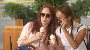 İki genç kadın açık bir kafede oturup dondurma yemek, eğleniyorlar. 4k, ağır çekim, steadicam.
