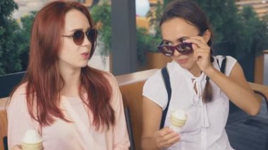 İki genç kadın açık bir kafede oturup dondurma yemek, eğleniyorlar. 4k, ağır çekim, steadicam.