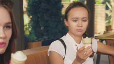İki genç kadın açık bir kafede oturup dondurma yemek, eğleniyorlar. 4k, ağır çekim, steadicam.