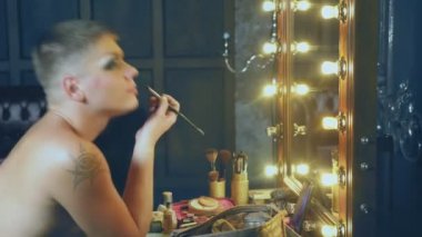 travesti-diva. Bir travesti kavramı. Adam-aktör bir kadına dönüşür. bir adam, yüzünde bir makyaj uygulanır. Aynanın önünde odaya. 4k, ağır çekim, steadicam çekim