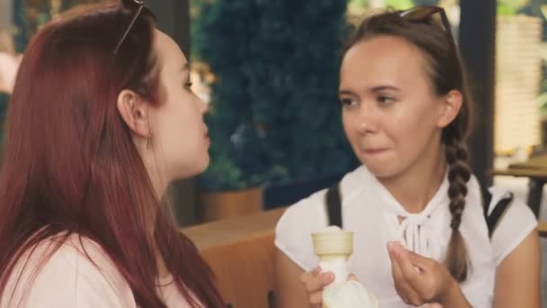 Deux jeunes femmes mangent de la crème glacée, assises dans un café extérieur, elles s'amusent. 4k, ralenti, steadicam . — Video