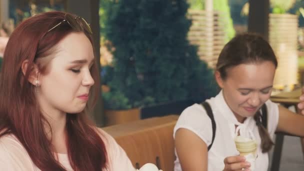 Två unga kvinnor äter glass, sitter i ett utomhus café, de har roligt. 4k, ultrarapid, steadicam. — Stockvideo