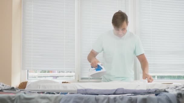 Jeune homme, debout derrière la planche en fer à repasser fumant, chemise à repasser pendant les travaux ménagers. 4k, au ralenti — Video