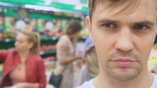 En el supermercado, un primer plano de la cara del marido que espera a su esposa mientras ella está de compras en la tienda. marido cansado aburrido. compras en pareja, 4k — Vídeos de Stock