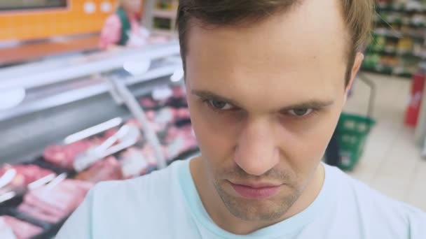 No supermercado, um close-up do rosto do marido que espera sua esposa enquanto ela está comprando na loja. entediado marido cansado. casal de compras, 4k — Vídeo de Stock