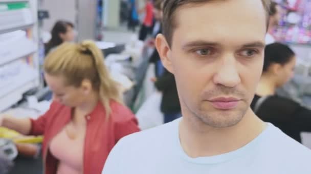 In de supermarkt, een close-up van het gezicht van de man die zijn vrouw verwacht terwijl ze is winkelen bij de store. verveeld moe man. paar winkelen, 4k — Stockvideo