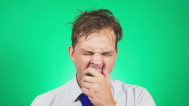Uykulu, darmadağınık genç adam bir takım elbise ve kravat, esner ve kameraya doğru görünüyor. 4k, yeşil renkli, ağır çekim. duygular