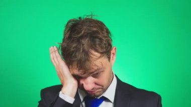 Uykulu, darmadağınık genç adam bir takım elbise ve kravat, esner ve kameraya doğru görünüyor. 4k, yeşil renkli, ağır çekim. duygular