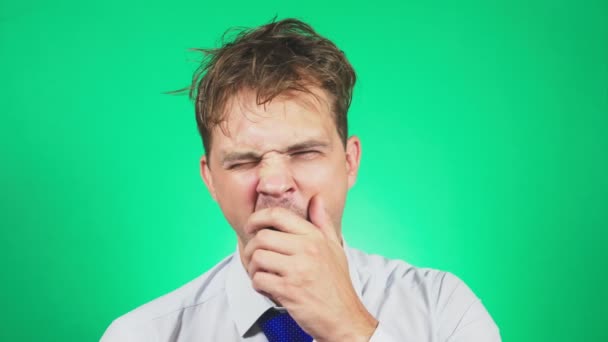 Slaperig, Verfomfaaid jonge man in een pak en stropdas, gaapt en kijkt naar de camera. 4k, groene achtergrond, slow-motion. emoties — Stockvideo