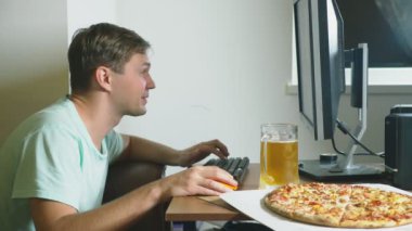 teknoloji, Oyunlar, eğlence, oyun ve insanlar kavramı. evde bir bilgisayar oyunu oynamak, bira içme ve pizza yemek genç bir adam. 4k, ağır çekim