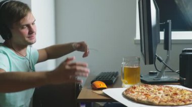 teknoloji, Oyunlar, eğlence, oyun ve insanlar kavramı. evde bir bilgisayar oyunu oynamak, bira içme ve pizza yemek genç bir adam. 4k, ağır çekim