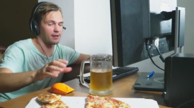 teknoloji, Oyunlar, eğlence, oyun ve insanlar kavramı. evde bir bilgisayar oyunu oynamak, bira içme ve pizza yemek genç bir adam. 4k, ağır çekim.