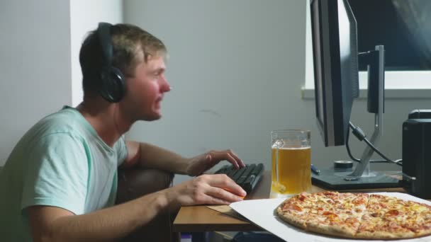 Tecnologia, jogos, entretenimento, jogo e conceito de pessoas. um jovem jogando um jogo de computador em casa, bebendo cerveja e comendo pizza. 4k, câmera lenta — Vídeo de Stock