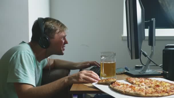 Tecnología, juegos, entretenimiento, juego y concepto de personas. un joven jugando un juego de ordenador en casa, bebiendo cerveza y comiendo pizza. 4k, cámara lenta — Vídeo de stock