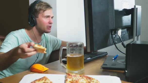 Technologie, jeux, divertissement, jeu et concept de personnes. un jeune homme jouant à un jeu informatique à la maison, buvant de la bière et mangeant de la pizza. 4k, au ralenti — Video