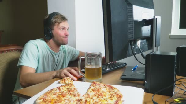 Tecnologia, giochi, intrattenimento, gioco e concetto di persone. un giovane che gioca a un gioco per computer a casa, beve birra e mangia pizza. 4k, rallentatore — Video Stock
