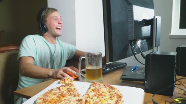 Tecnologia, giochi, intrattenimento, gioco e concetto di persone. un giovane che gioca a un gioco per computer a casa, beve birra e mangia pizza. 4k, rallentatore — Video Stock