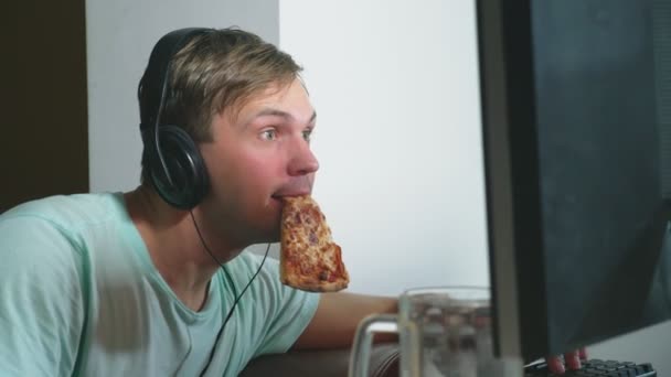 Технологии, игры, развлечения, игра и концепция людей. Молодой человек играет в компьютерную игру дома, пьет пиво и ест пиццу. 4k, slow motion — стоковое видео