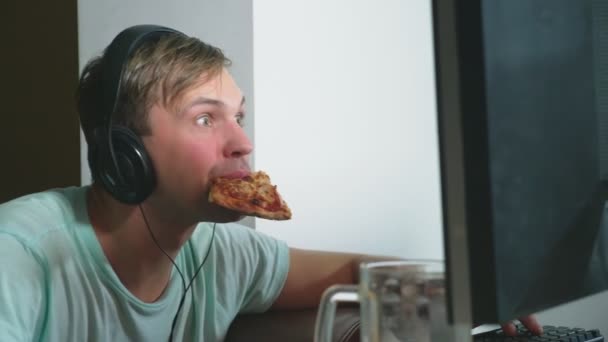 Tecnologia, jogos, entretenimento, jogo e conceito de pessoas. um jovem jogando um jogo de computador em casa, bebendo cerveja e comendo pizza. 4k, câmera lenta — Vídeo de Stock