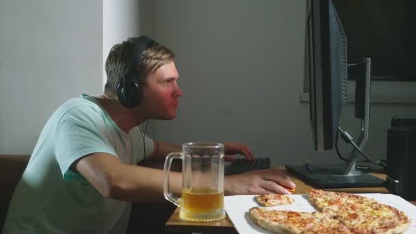 Технології, ігри, розваги, гра та концепція людей. молодий чоловік грає в комп'ютерну гру вдома, п'є пиво і їсть піцу. 4k, повільний рух — стокове відео