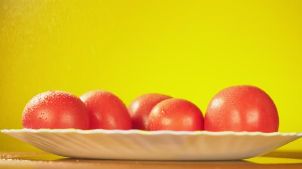 I pomodori freschi cadono con gocce d'acqua su un piatto. Il concetto di nutrizione. Isolato su uno sfondo giallo, rallentamento — Video Stock
