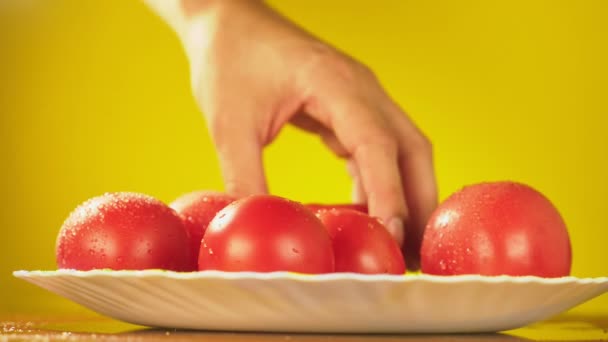 A mão leva tomates frescos com gotas de água do prato. O conceito de nutrição. Isolar em um fundo amarelo, abrandamento — Vídeo de Stock