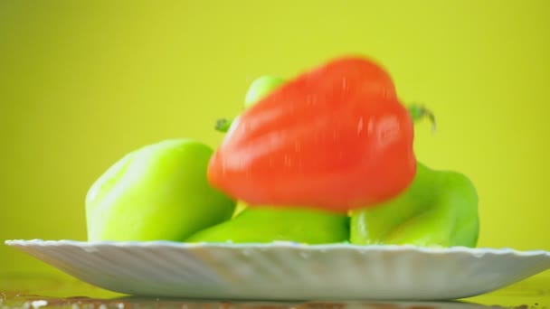Φρέσκες πιπεριές Balgar πέφτουν με νερό σε ένα πιάτο. Η έννοια της διατροφής. Απομόνωση σε κίτρινο φόντο, επιβράδυνση. — Αρχείο Βίντεο
