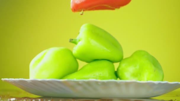 Φρέσκες πιπεριές Balgar πέφτουν με νερό σε ένα πιάτο. Η έννοια της διατροφής. Απομόνωση σε κίτρινο φόντο, επιβράδυνση. — Αρχείο Βίντεο