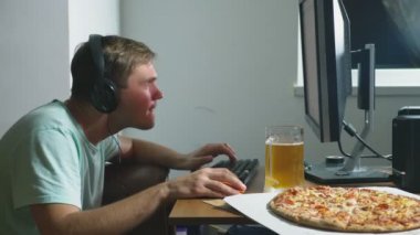 teknoloji, Oyunlar, eğlence, oyun ve insanlar kavramı. evde bir bilgisayar oyunu oynamak, bira içme ve pizza yemek genç bir adam. 4k, ağır çekim