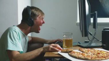 teknoloji, Oyunlar, eğlence, oyun ve insanlar kavramı. evde bir bilgisayar oyunu oynamak, bira içme ve pizza yemek genç bir adam. 4k, ağır çekim