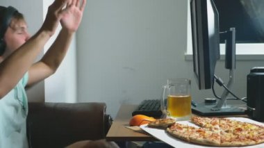 teknoloji, Oyunlar, eğlence, oyun ve insanlar kavramı. evde bir bilgisayar oyunu oynamak, bira içme ve pizza yemek genç bir adam. 4k, ağır çekim