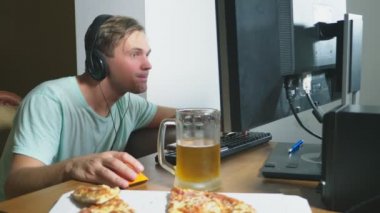 teknoloji, Oyunlar, eğlence, oyun ve insanlar kavramı. evde bir bilgisayar oyunu oynamak, bira içme ve pizza yemek genç bir adam. 4k, ağır çekim