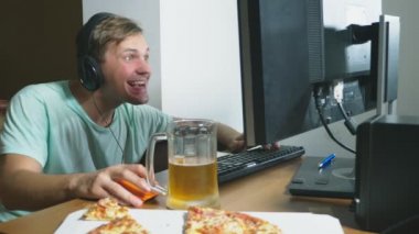 teknoloji, Oyunlar, eğlence, oyun ve insanlar kavramı. evde bir bilgisayar oyunu oynamak, bira içme ve pizza yemek genç bir adam. 4k, ağır çekim