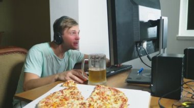 teknoloji, Oyunlar, eğlence, oyun ve insanlar kavramı. evde bir bilgisayar oyunu oynamak, bira içme ve pizza yemek genç bir adam. 4k, ağır çekim