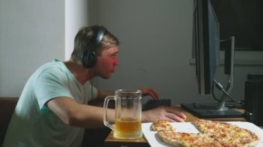 teknoloji, Oyunlar, eğlence, oyun ve insanlar kavramı. evde bir bilgisayar oyunu oynamak, bira içme ve pizza yemek genç bir adam. 4k, ağır çekim