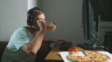 teknoloji, Oyunlar, eğlence, oyun ve insanlar kavramı. evde bir bilgisayar oyunu oynamak, bira içme ve pizza yemek genç bir adam. 4k, ağır çekim