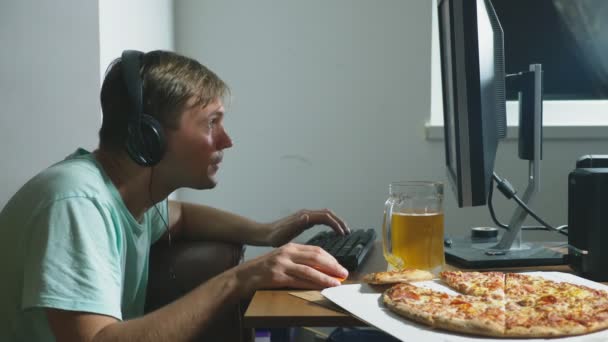 Technologie, hry, zábava, hry a lidé koncept. mladý muž hraje počítačovou hru doma, pít pivo a jíst pizzu. 4k, pomalý pohyb — Stock video