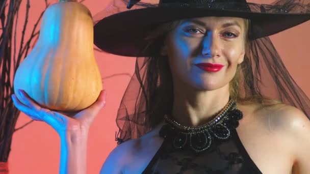 Красивая молодая сексуальная женщина в черном костюме ведьмы и шляпе, с тыквой в руках. скопировать пространство. 4k, slow motion — стоковое видео