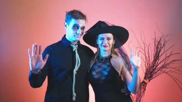 Beau couple, homme et femme en costumes de sorcière et halloween zombie, 4k, tir au ralenti, agitant les mains en regardant la caméra. félicitations pour les vacances — Video