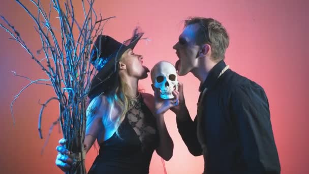 A beautiful couple, a man and a woman in witch and zombie costumes for Halloween, 4k, slow-motion, hold the skull in their hands. congratulation on the holiday, — Stock Video