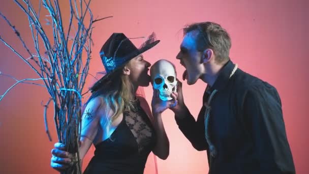 A beautiful couple, a man and a woman in witch and zombie costumes for Halloween, 4k, slow-motion, hold the skull in their hands. congratulation on the holiday, — Stock Video
