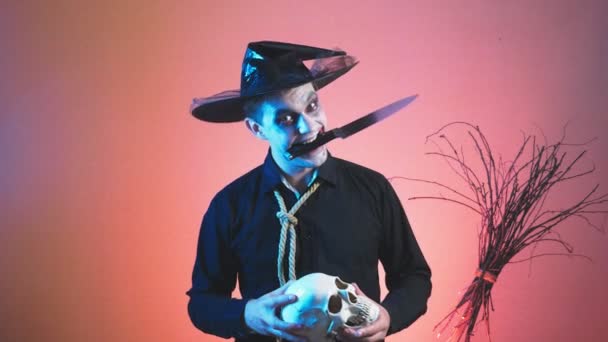 Een jonge man in een zombie kostuum voor halloween, met een schedel in zijn handen. 4k, slow-motion. Close-up — Stockvideo