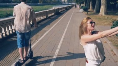 güzel mutlu kadın blogger bir kamera ile ona röportaj resort şehir set strolling yol açar. rüzgar saçlarını ağaçların dalları ile güneş ışığı glintes geliştirir