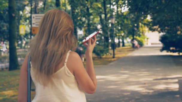 Mujer joven y feliz hablando por teléfono, caminando por el paseo marítimo en un caluroso día soleado de verano. 4k, cámara lenta — Vídeos de Stock